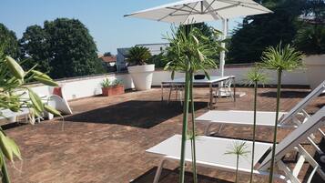 Un patio en la azotea con sillones blancos, una mesa y plantas en macetas.