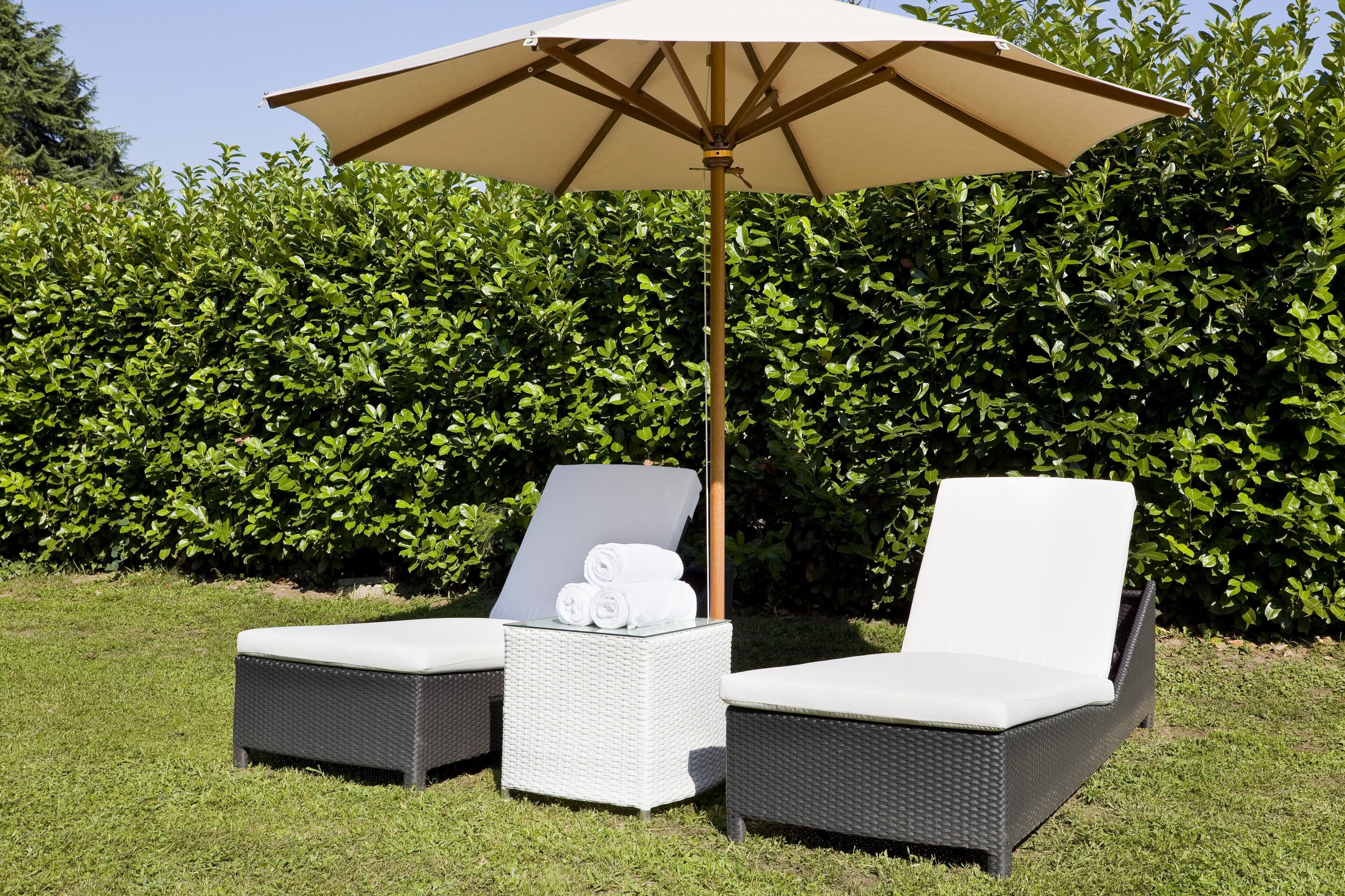 A garden area with two wicker lounge chairs and a table, each with a white cushion. An umbrella provides shade.