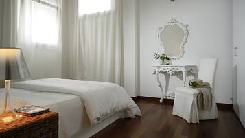 Quarto com cama, mesa de cabeceira com abajur, uma mesinha de canto com espelho e uma cadeira.
