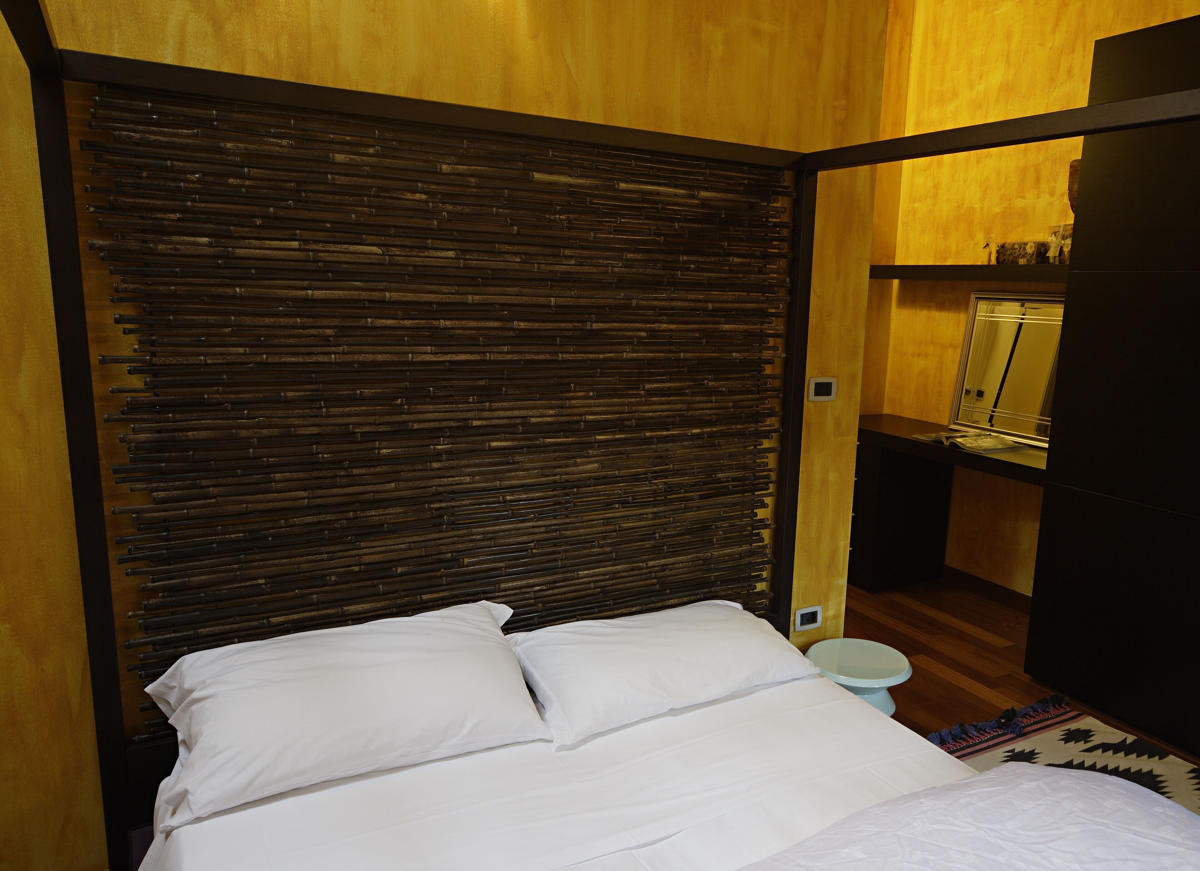 A bedroom with a bed, wooden headboard, and a small bedside table with a mirror.