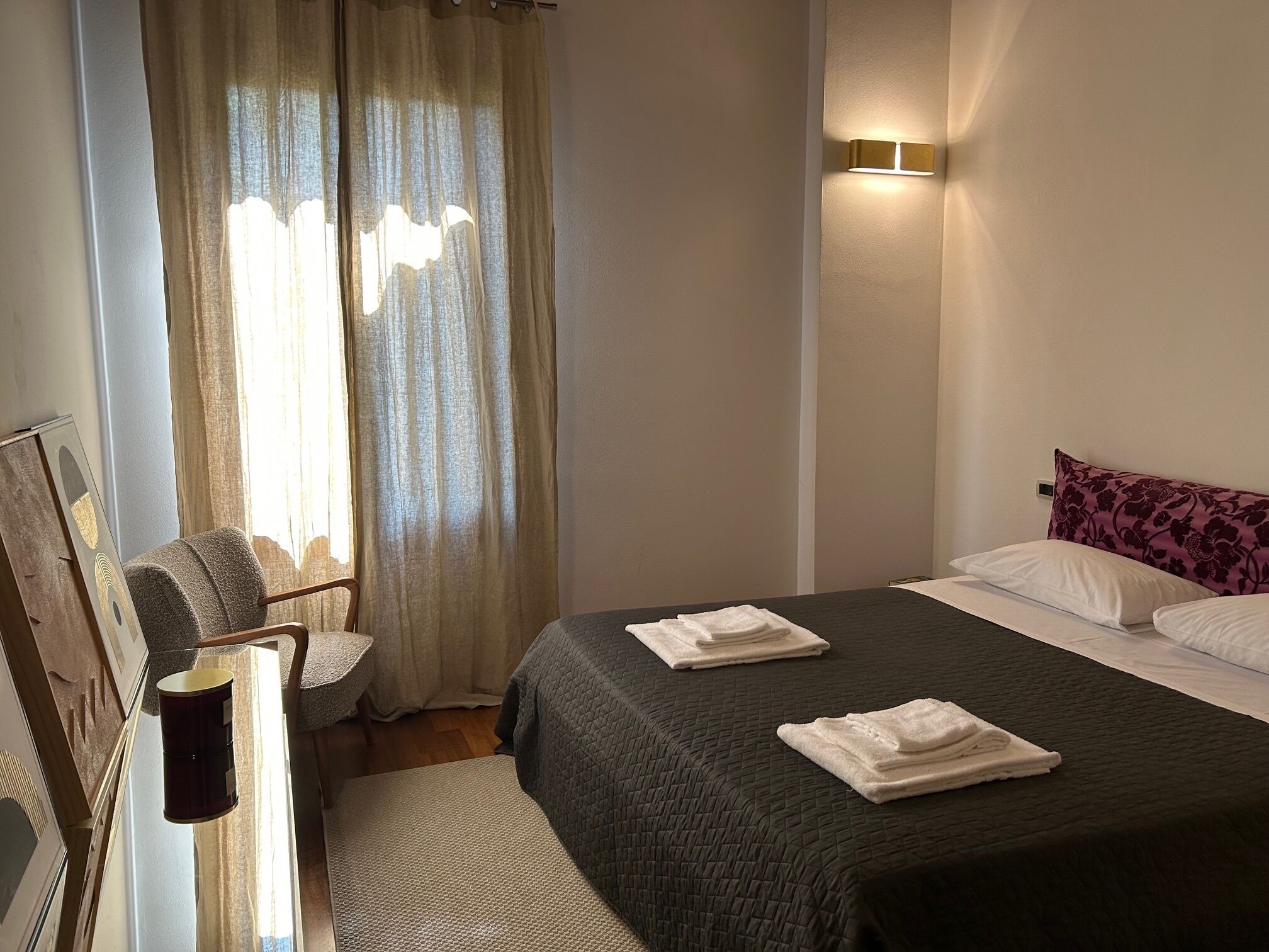 A hotel room with a bed, a chair, a desk, and a window with curtains.