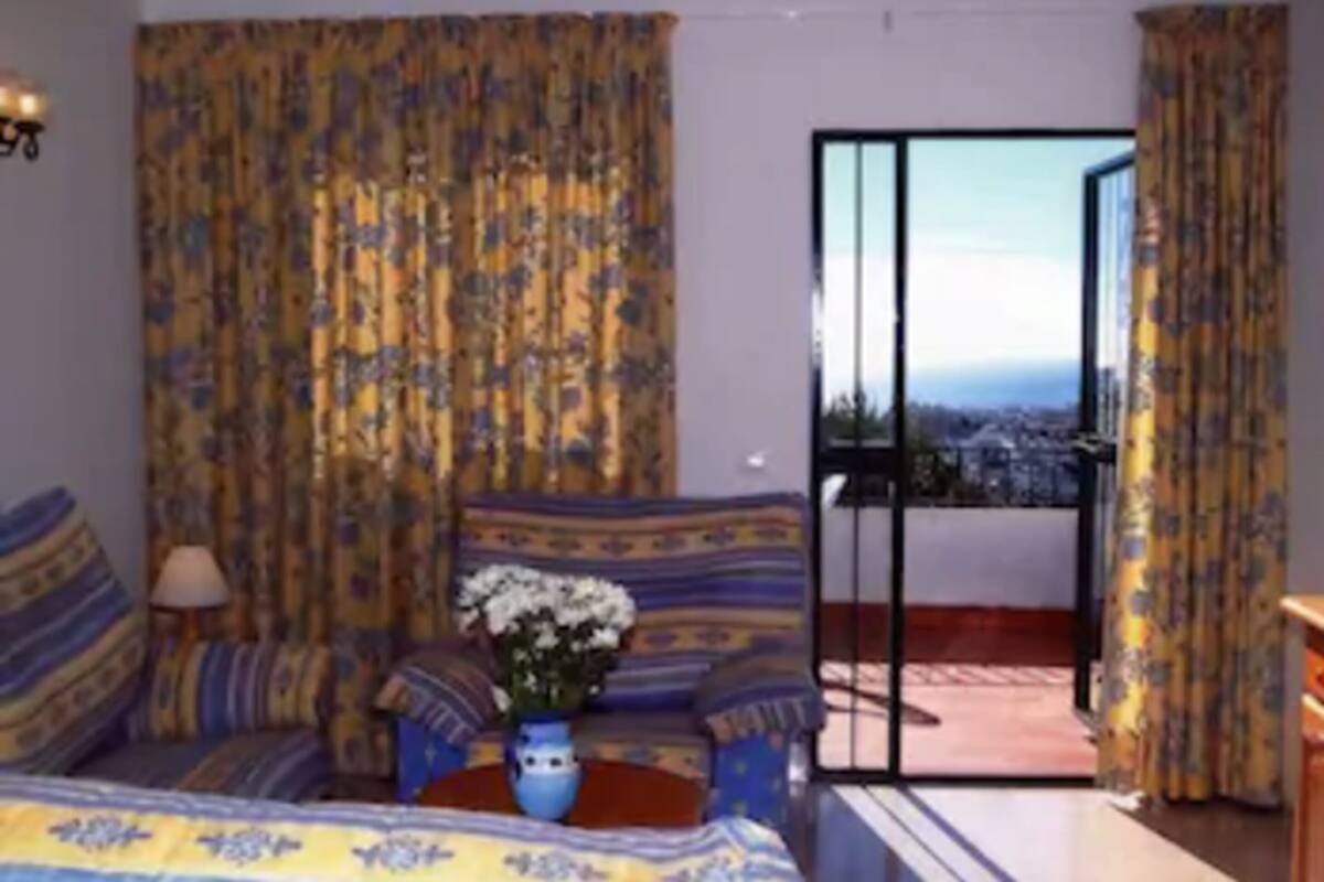 A room with a bed, a small table with a vase, and a view through a glass door.