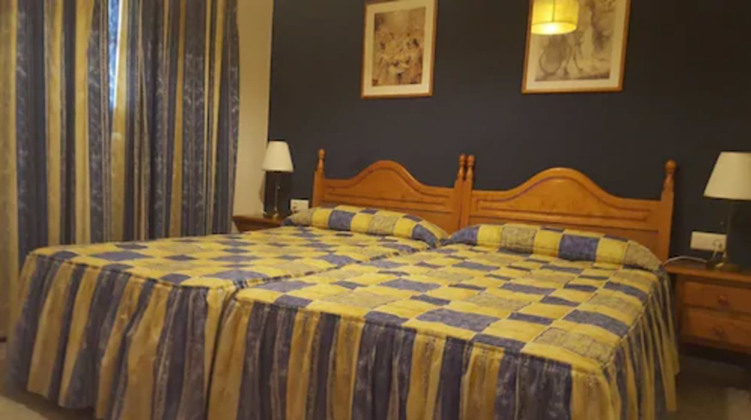 Una cama doble con colcha de cuadros, dos lámparas de noche y una mesita.