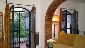 Quarto com sofá amarelo, uma mesa com um vaso e vista para área externa através de uma porta de vidro.