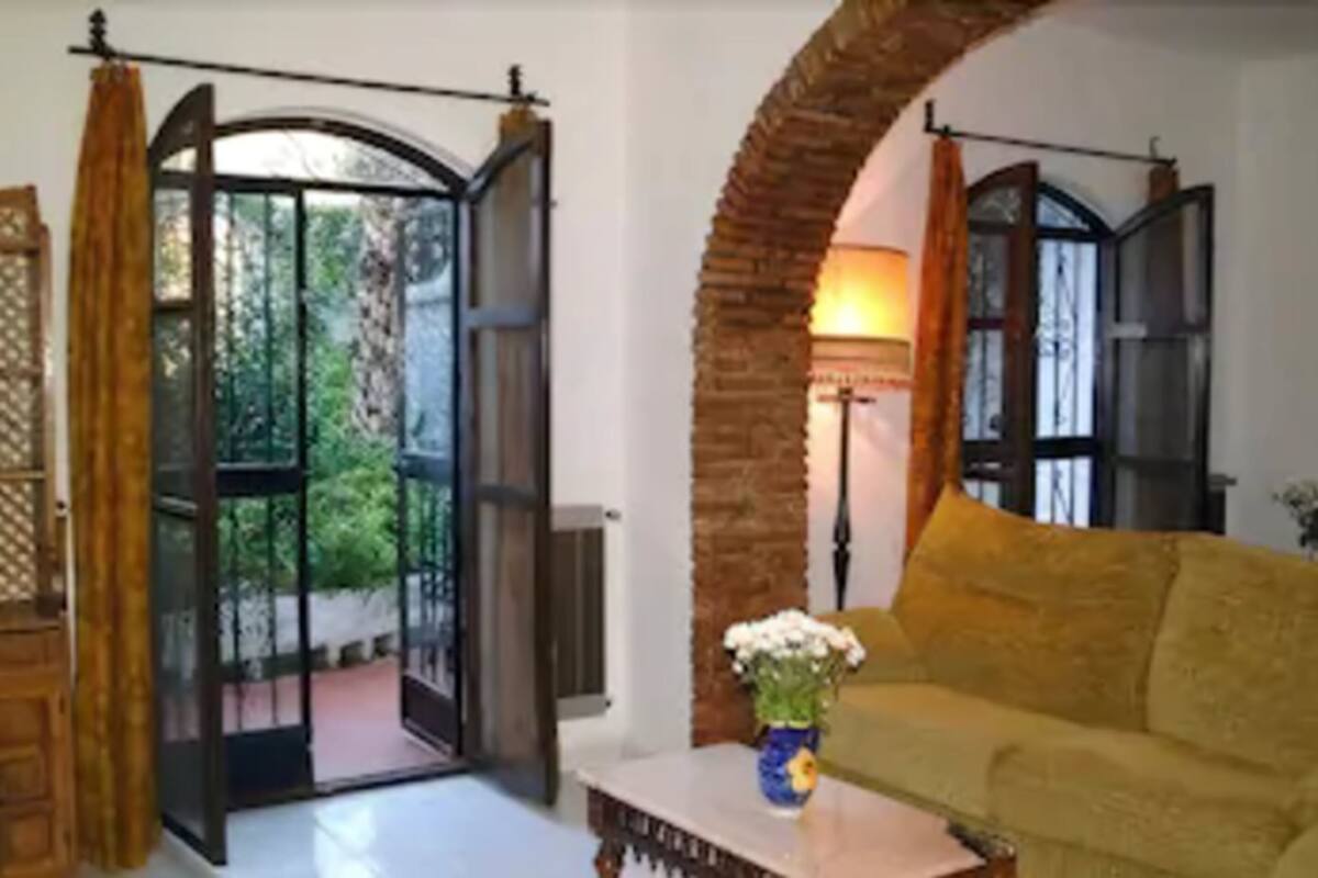 A room with a yellow sofa, a table with a vase, and a view through a glass door to an outdoor area.