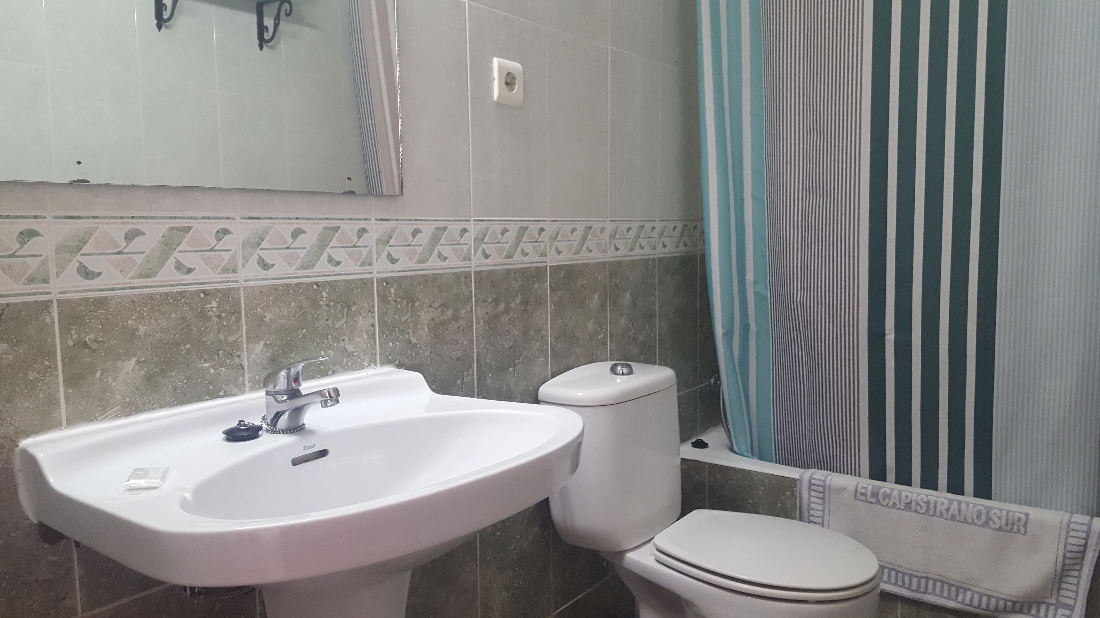 A bathroom with a white sink, toilet, and a striped shower curtain.
