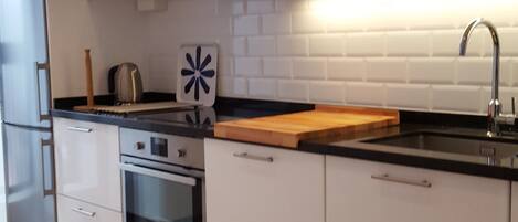 A modern kitchen with white cabinets, a black countertop, a microwave, an oven, and a sink.