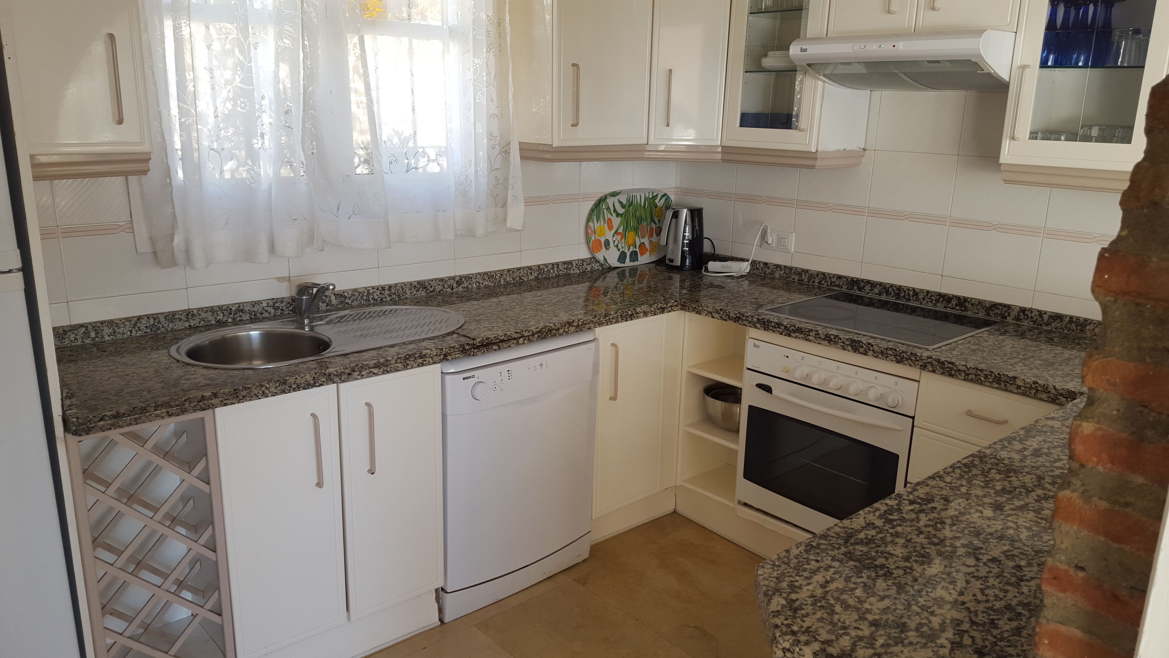 Una cocina con armarios blancos, encimera de granito, horno empotrado y lavavajillas.