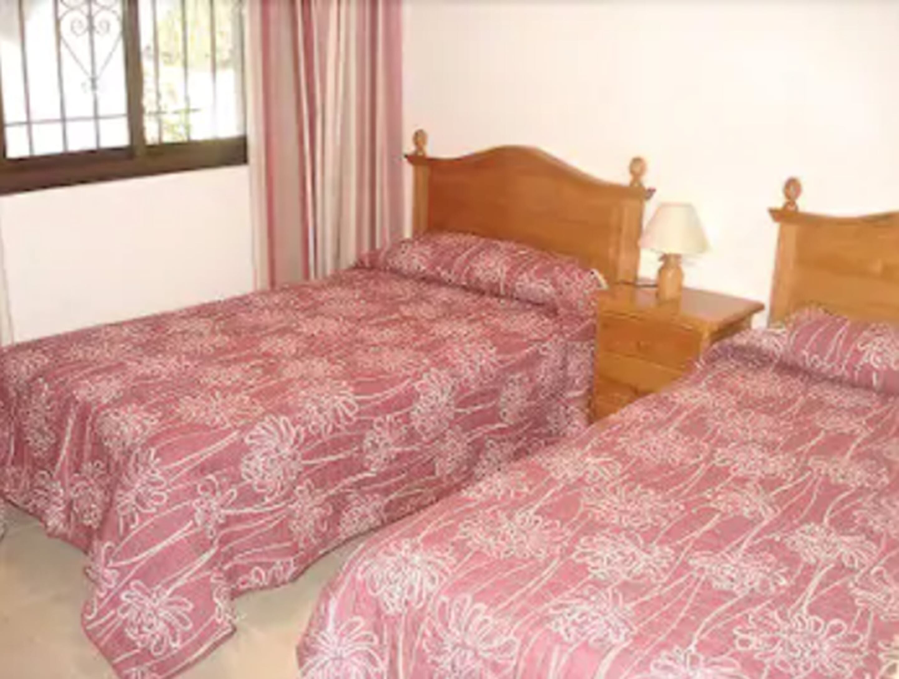 A bedroom with two single beds, each with a wooden headboard and a bedside table with a lamp.