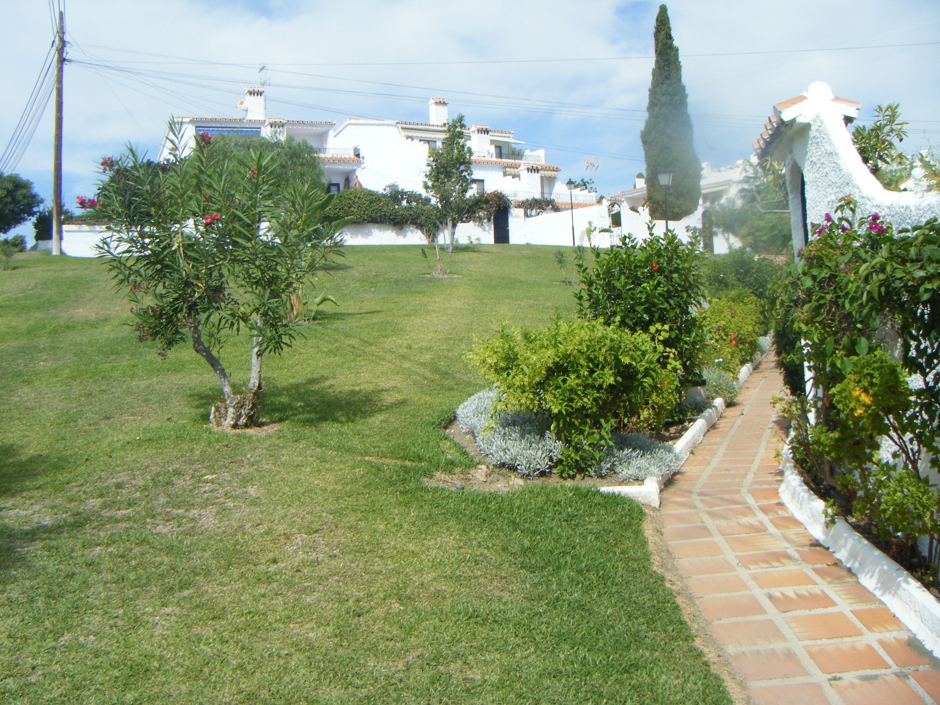 A grassy area with a pathway leading to a building with white walls and a tiled roof.