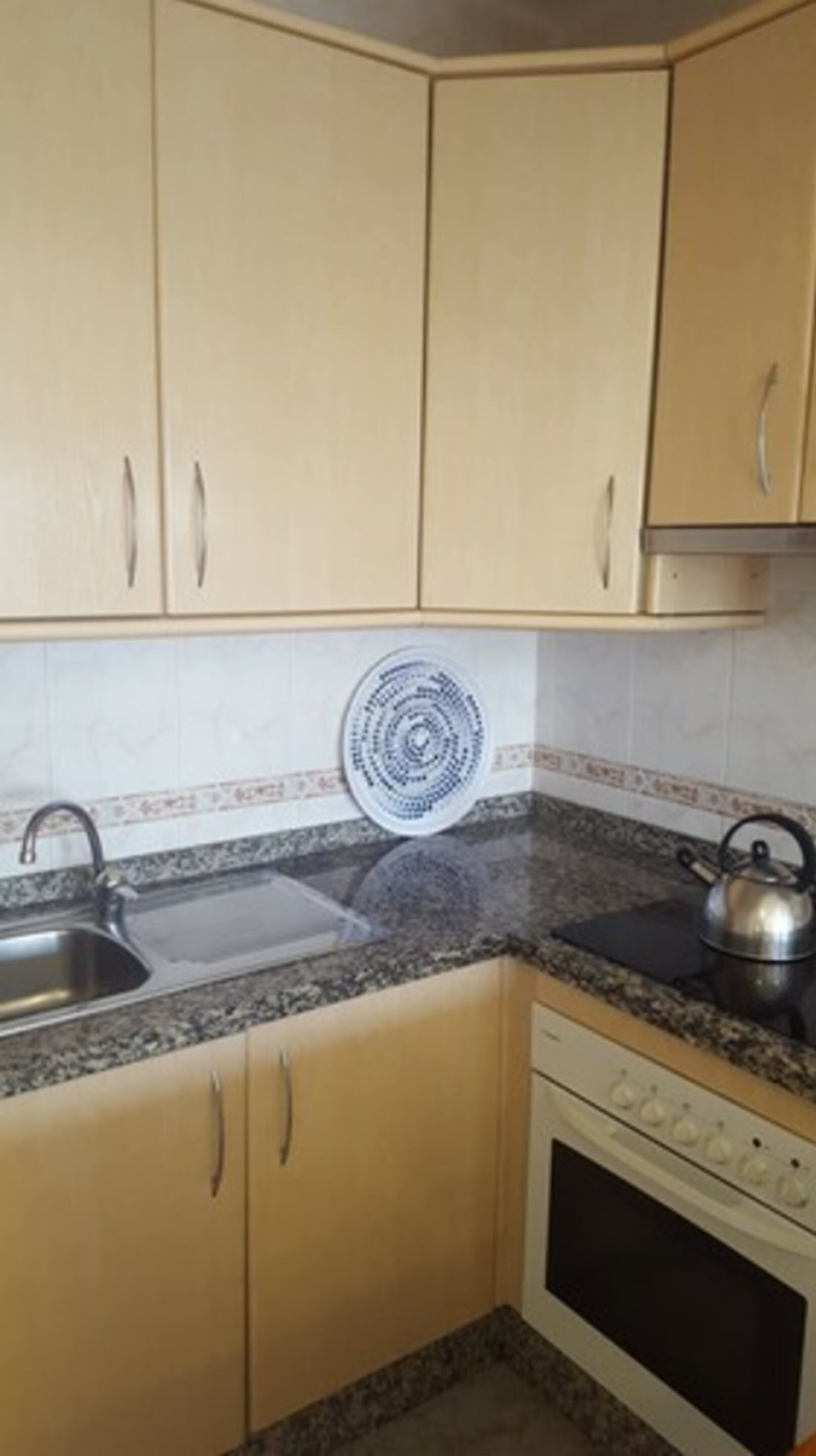 Uma cozinha com armários bege, bancada de granito, pia, fogão e um prato decorativo na parede.