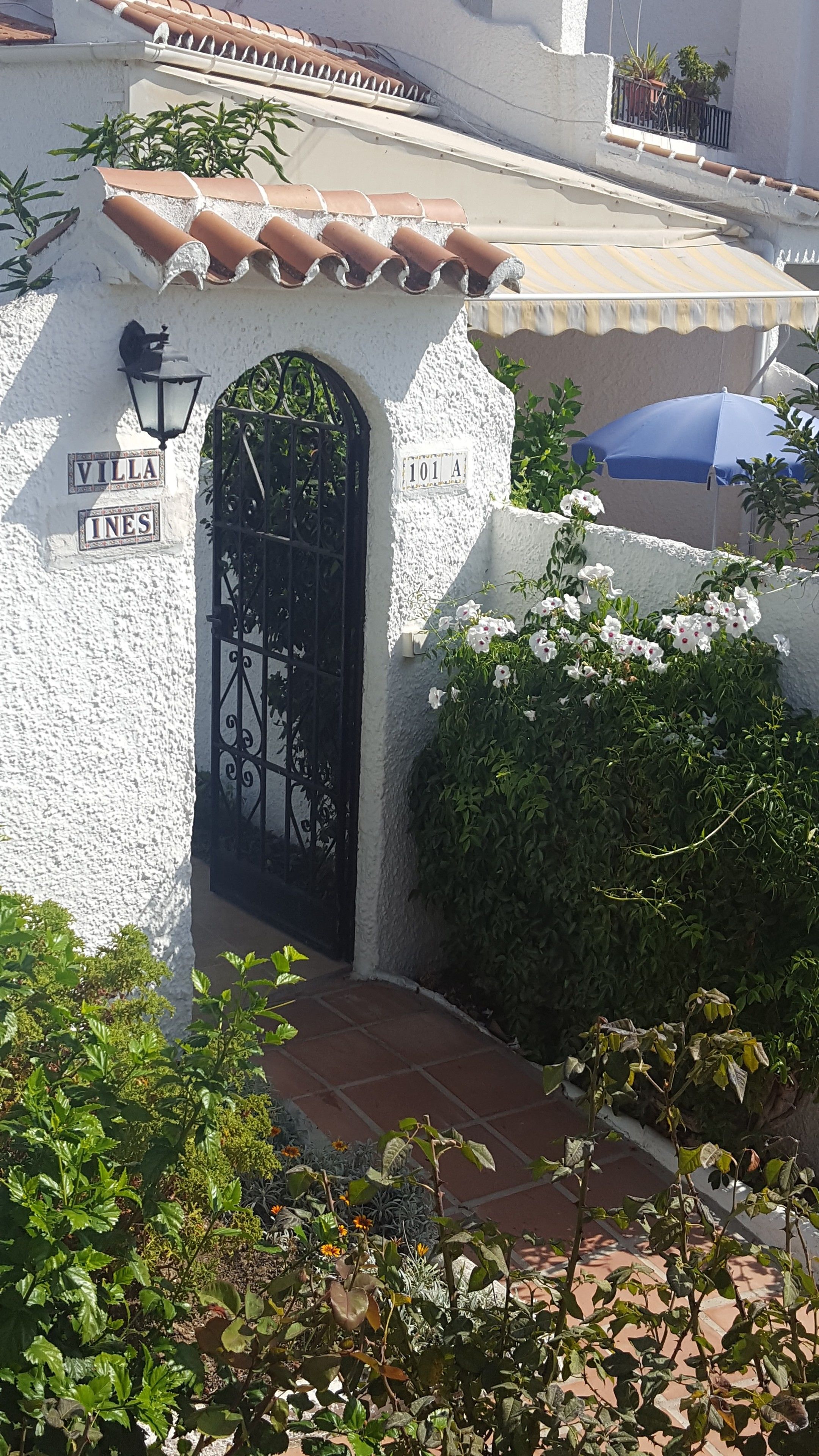 Una villa con facciata bianca, un cancello nero e un cartello con la scritta 'VILLA INES 101 A'.
