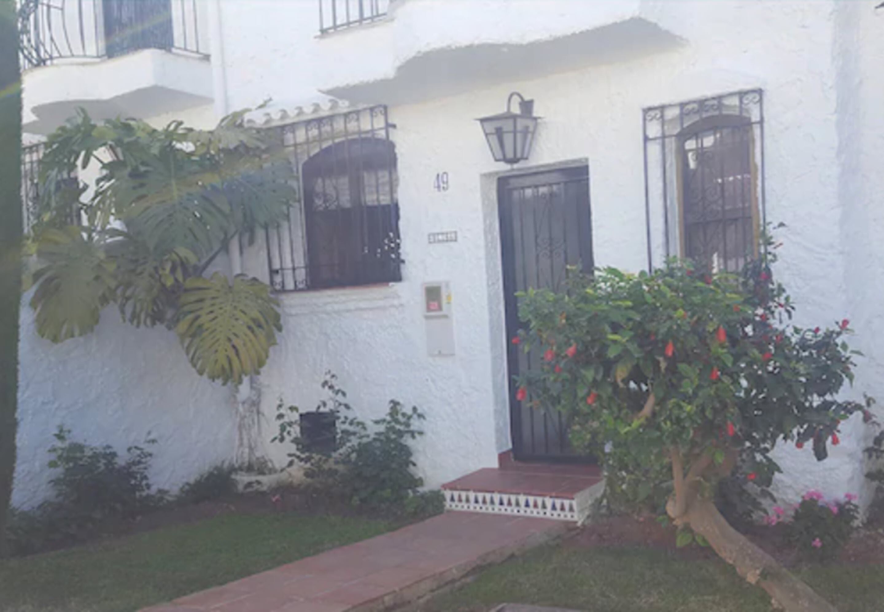 Un edificio blanco con una puerta negra, una ventana con reja metálica y un pequeño porche con escalones.