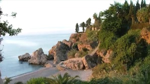 Paisagem costeira com terreno rochoso, vegetação e uma praia.
