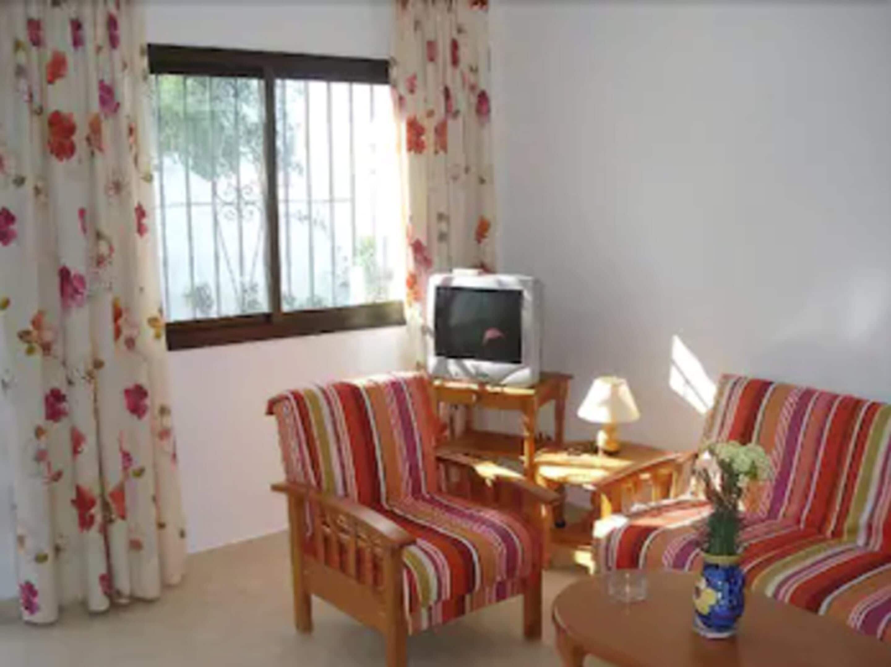 A living room with a sofa, armchair, TV, lamp, and a small table.