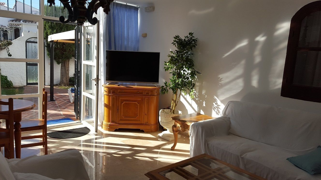 Una sala de estar con televisor, sofá, mesa de centro y mesa de comedor.