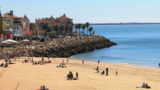 A beach with people, a rocky breakwater, and buildings in the background. - Apartamentos Puerto Sherry (El Puerto de Santa Maria)