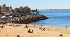A beach with people, a rocky breakwater, and buildings in the background.