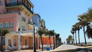 A coastal street with colorful buildings, outdoor seating, and palm trees. - Apartamentos Puerto Sherry (El Puerto de Santa Maria)