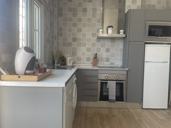 Cocina compacta con baldosas grises, microondas, refrigerador de dos puertas y horno pequeño.