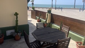 A patio with a wooden table and chairs, potted plants, and a view of the beach and ocean. - Apartamentos Puerto Sherry (El Puerto de Santa Maria)