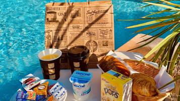 Preparació al costat de la piscina amb una bossa de paper, gots de cafè, iogurt Danone, cereals Kellogg's i un cistell de pa.
