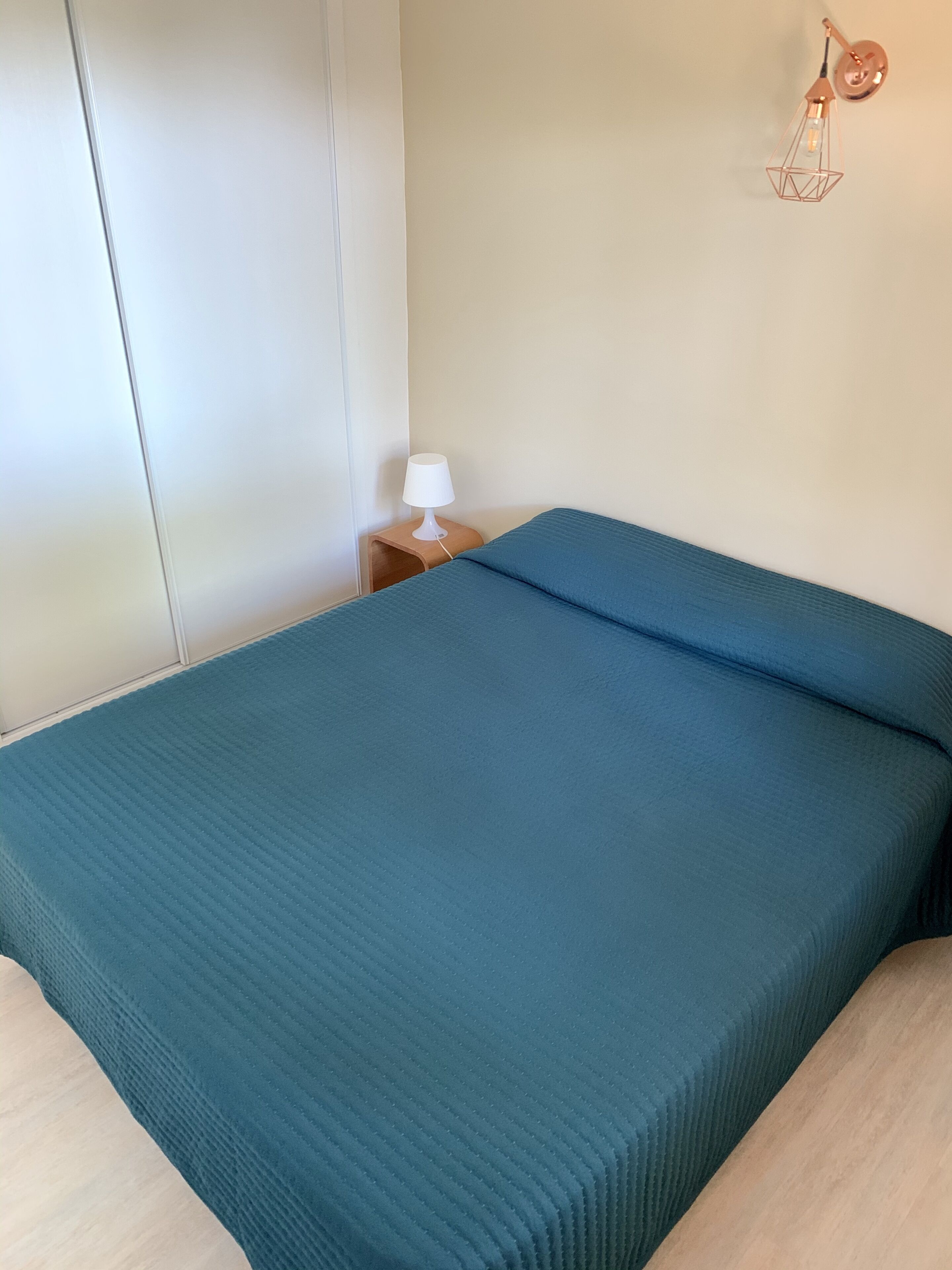 A room with a bed, a nightstand with a lamp, and a wall-mounted light fixture.