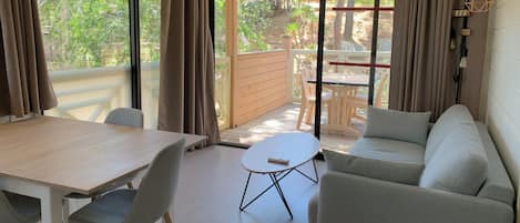 Una habitación moderna con una mesa de madera, sillas grises, un sofá blanco y una pequeña mesa redonda.