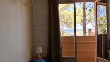 Un dormitorio con cama, una mesita de noche con lámpara, ventana con cortinas y vistas a árboles y un edificio.