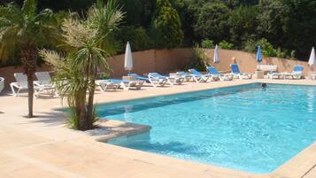 A swimming pool with lounge chairs and umbrellas, surrounded by palm trees and hedges.
