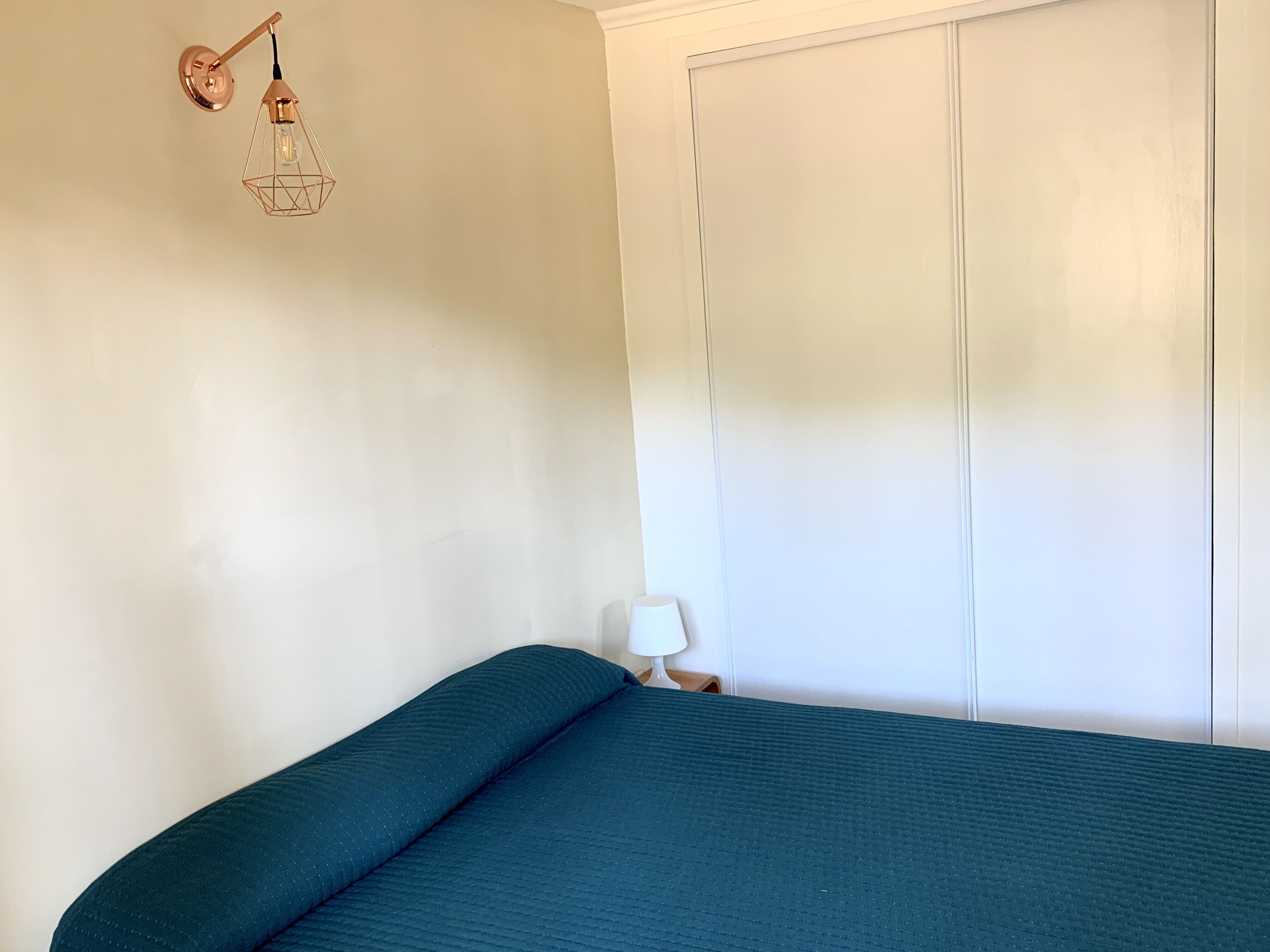 Un dormitorio con cama, mesita de noche, lámpara y una lámpara fijada a la pared.