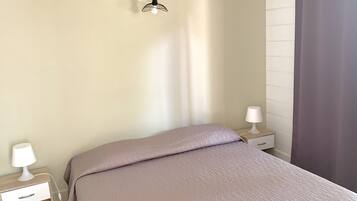 A bedroom with a bed, two bedside tables with lamps, a wall-mounted light fixture, and a window with a curtain.