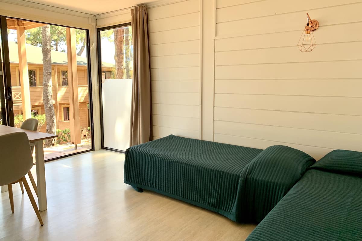 A room with a bed, a table, and a chair. There is a window with a view of buildings outside.