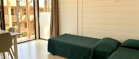 A room with a bed, a table, and a chair. There is a window with a view of buildings outside.