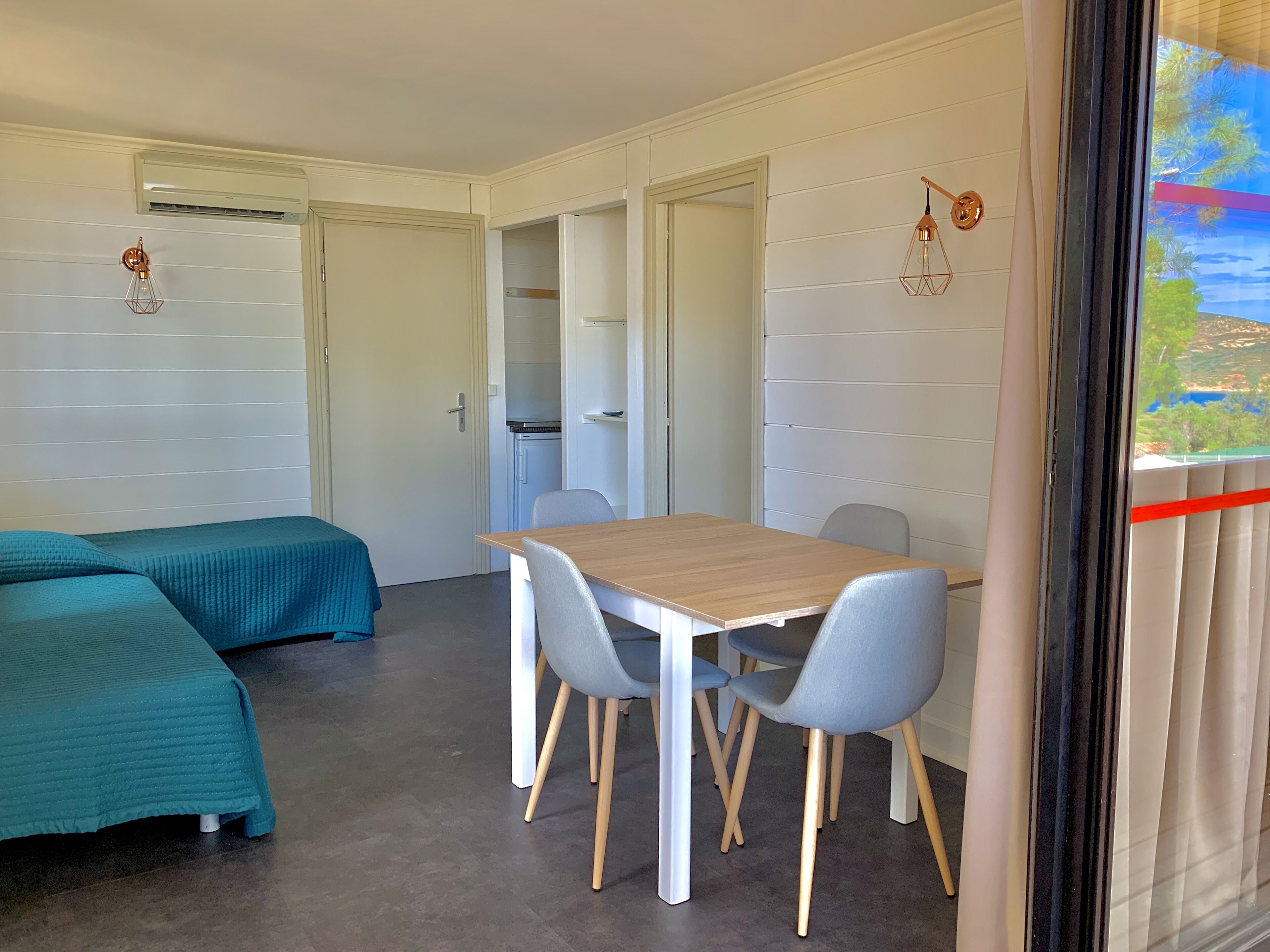 Una habitació amb un llit, una taula, cadires, una porta i una finestra amb vistes.