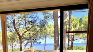A wooden deck with a table and chairs, overlooking a body of water and trees. - Résidence Les Pins (Calvi)
