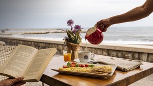 A breakfast setup with a book, a plate of food, a cup, and a glass of orange juice on a table by the sea. - Hotel La Chancla (Málaga)