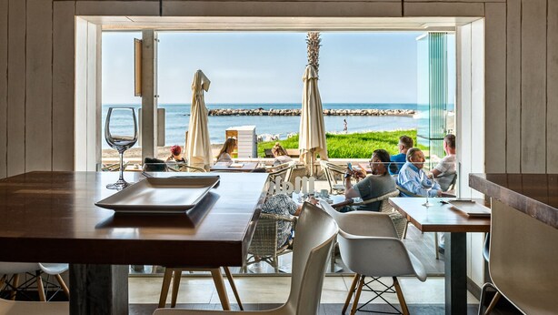 A dining area with a view of the sea, featuring tables and chairs, umbrellas, and a wooden interior. - Hotel La Chancla (Málaga)