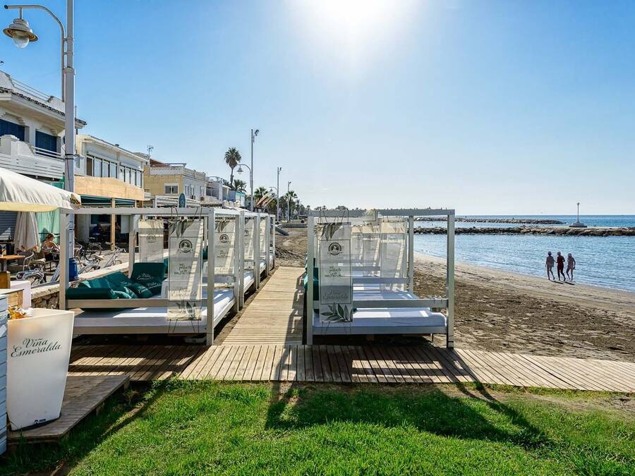 A beachside hotel with outdoor seating and wooden deck beds overlooking the sea.