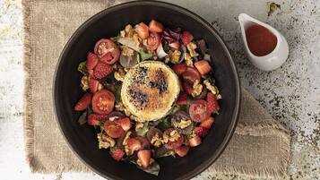 Ensalada con fresas, nueces y una rebanada de pan a la parrilla, acompañada de un recipiente pequeño con salsa.