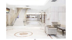 Un moderno vestíbulo de hotel con una escalera de mármol, un mostrador de recepción y una zona de estar con sofás.