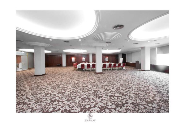 A spacious conference room with a patterned carpet, white pillars, and a long table with red chairs.