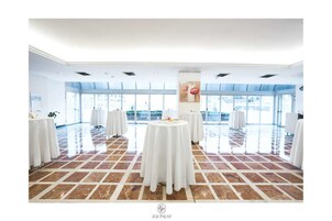 A spacious room with large windows, white tables, and a tiled floor.