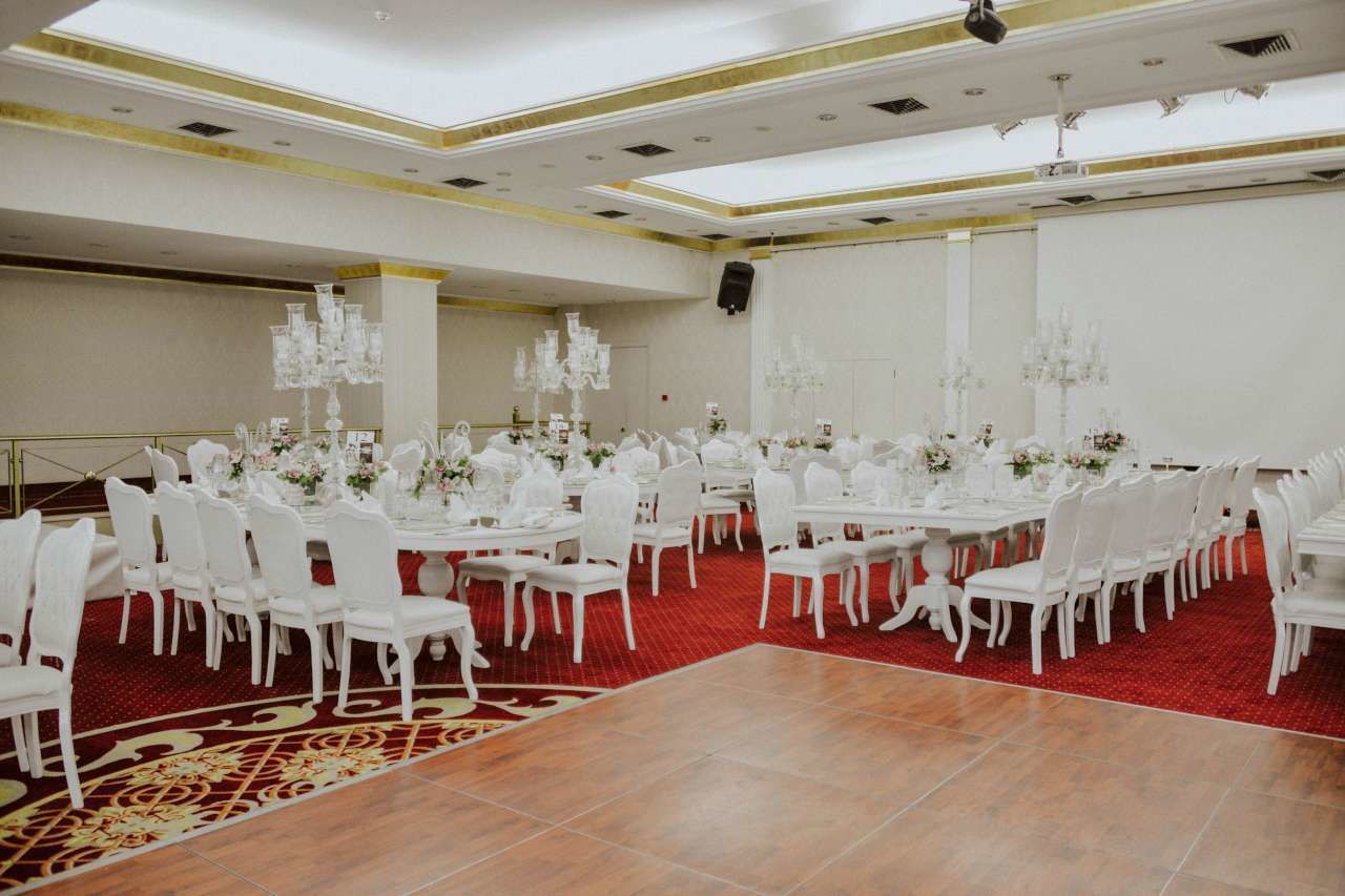 Une salle de banquet avec des tables rondes, des chaises blanches et des lustres.