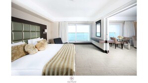 A hotel room with a large bed, a desk, and a view of the sea. - Ege Palas Business Hotel (Izmir)