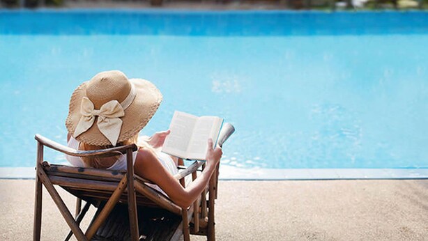 A person sitting in a chair by a pool, reading a book. - Ege Palas Business Hotel (Izmir)
