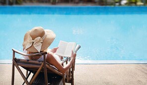 A person sitting in a chair by a pool, reading a book.