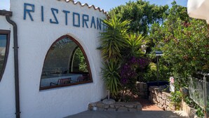 A restaurant with a white exterior, a large arched window, and a sign that reads "RISTORANTE". - AHR Altura Hotel Porto Rafael (Palau)