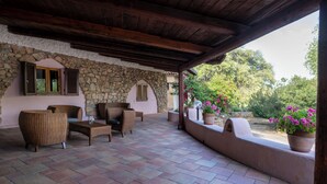 A covered patio area with stone walls, wicker furniture, and potted plants. - AHR Altura Hotel Porto Rafael (Palau)