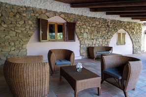 Un patio con paredes de piedra, mobiliario de mimbre y una mesa.